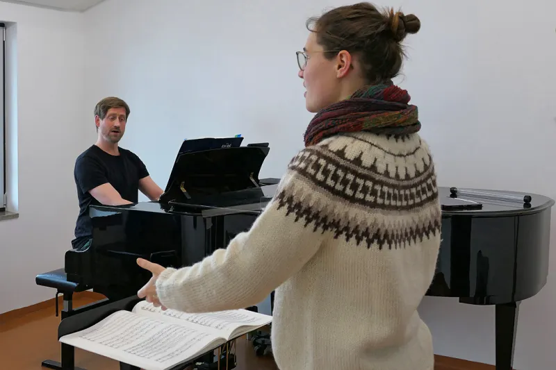 Studierende steht am Notenpult, Dozierende begleitet am Flügel